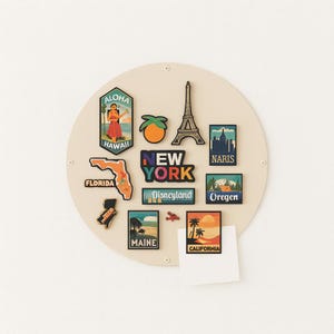May include: A collection of travel-themed magnets, including shapes of Florida, Hawaii, and Maine, plus magnets with the Eiffel Tower, and the text "New York" and "Disneyland". The magnets are arranged on a beige circular board.