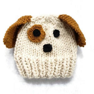 May include: A white knitted hat with brown ears and black eyes, resembling a dog.