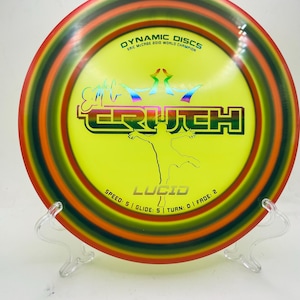 May include: A yellow Dynamic Discs disc with a red, orange, and green rim. The disc features the text "TRUTH" in a green outlined font, and "LUCID" below a silhouette of a person. The disc also has the text "ERIC MCCABE 2010 WORLD CHAMPION".