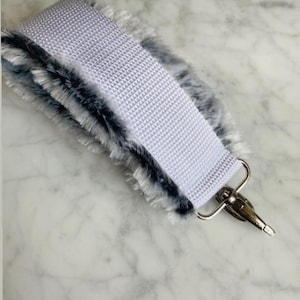 Puede incluir: Una correa de tracción con un centro tejido blanco y un borde de piel sintética gris y negra. Un cierre de metal plateado está unido al extremo. El texto "Pull straps May 14, 2022" es visible en la imagen.