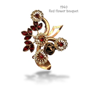 May include: Vintage 1940s gold-tone brooch in the shape of a red flower bouquet. The brooch features red and clear crystal accents, with a dark rose center. The text "1940 Red flower bouquet" is visible.