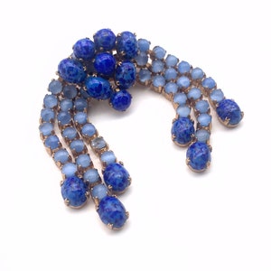 May include: A vintage brooch with a cluster of blue and light blue rhinestones. The brooch is shaped like a teardrop and has a gold tone finish.