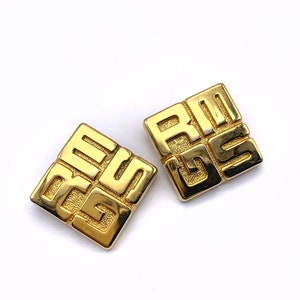 May include: A pair of gold-tone square earrings with a geometric design. The earrings feature the interlocking 'G' logo of the brand Givenchy.