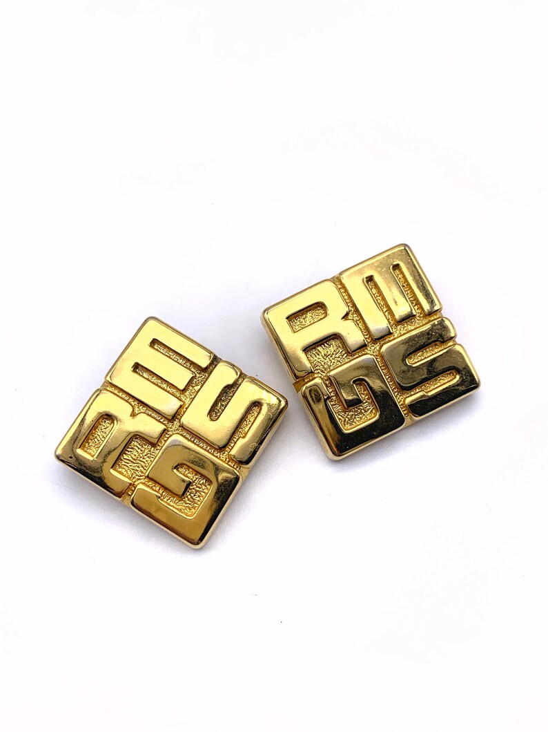 May include: A pair of gold-tone square earrings with a geometric design. The earrings feature the interlocking 'G' logo of the brand Givenchy.