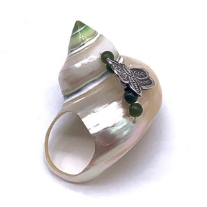 May include: A seashell ring with a green and white swirl pattern. The ring is decorated with a silver butterfly charm and green beads.