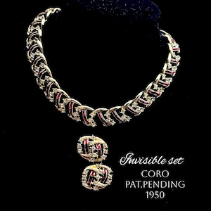 Könnte beinhalten: Ein goldfarbenes Halsketten- und Ohrring-Set mit roten und klaren Strasssteinen. Die Halskette ist eine Kette mit einem sich wiederholenden Muster aus roten und klaren Steinen. Die Ohrringe sind klein und rund mit einem ähnlichen Muster. Das Set ist mit "Invisible set CORO PAT.PENDING 1950" gekennzeichnet.
