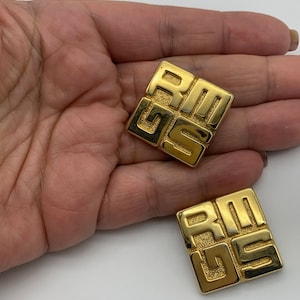 May include: A pair of gold-tone square-shaped earrings with the letters "Givenchy" embossed on them.