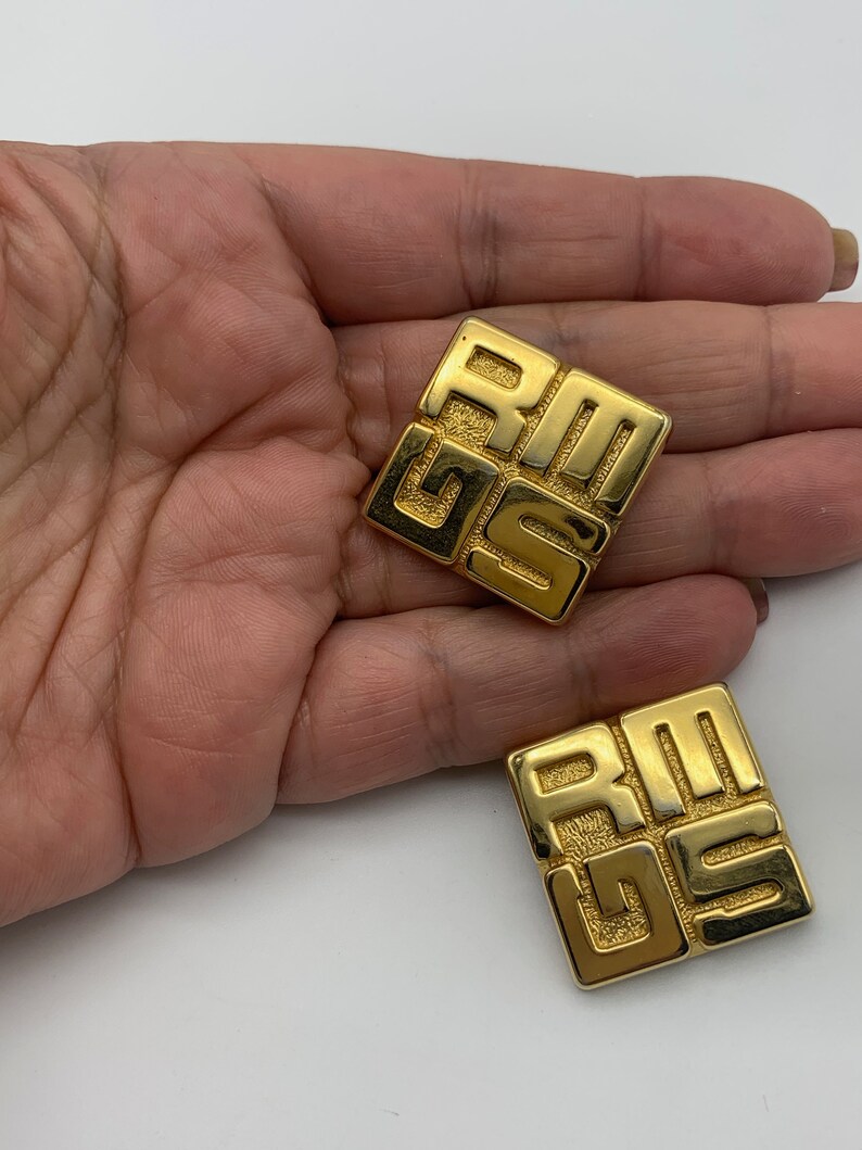 May include: A pair of gold-tone square-shaped earrings with the letters "Givenchy" embossed on them.