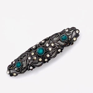 May include: A vintage brooch with a filigree design featuring a dark metal base and green and clear rhinestones.