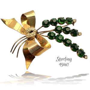 May include: A gold bow brooch with a cluster of green rhinestones. The brooch is marked "Sterling 1940".