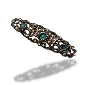 May include: A silver-toned brooch with a delicate floral design and three green glass stones.