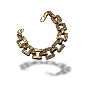Könnte beinhalten: Ein goldenes Kettenarmband mit einem klobigen Gliederdesign. Die Glieder sind mit kleinen, klaren Strasssteinen verziert.