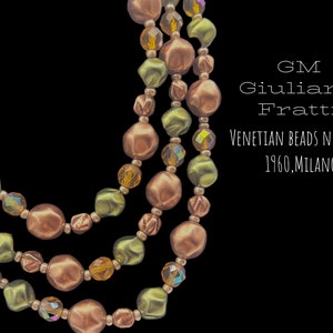 May include: A three-strand Venetian beads necklace in shades of olive green, copper, and amber. The necklace features various bead shapes and sizes, with iridescent accents. Text on the right reads: GM Giuliano Fratti, Venetian Beads Necklace, 1960, Milano.