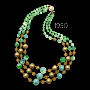 May include: A vintage three-strand necklace with green, gold, and blue beads. The necklace features a mix of small and large beads, with a decorative clasp. The text "1950" is visible in the image.