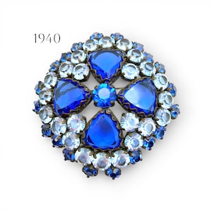Könnte beinhalten: Vintage Brosche mit blauen Strasssteinen und einem zentralen Kreuzdesign. Die Brosche hat große, facettierte blaue Steine, die von kleineren, hellblauen und klaren Strasssteinen umgeben sind. Der Text "1940" befindet sich in der oberen linken Ecke.