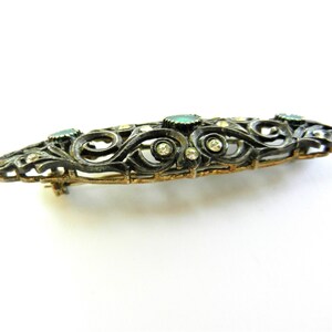 May include: A silver and gold filigree brooch with green and clear stones.