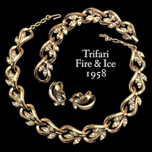 Op de afbeelding: Een gouden ketting en oorbellenset met heldere strasssteentjes. De ketting heeft een bladontwerp en de oorbellen zijn clip-on. De set is gemarkeerd met "Trifari Fire & Ice 1958".