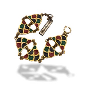 May include: A gold-tone bracelet with a geometric design featuring red, green, and black enamel. The bracelet has a clasp and a tag that reads "Rita Fashions".