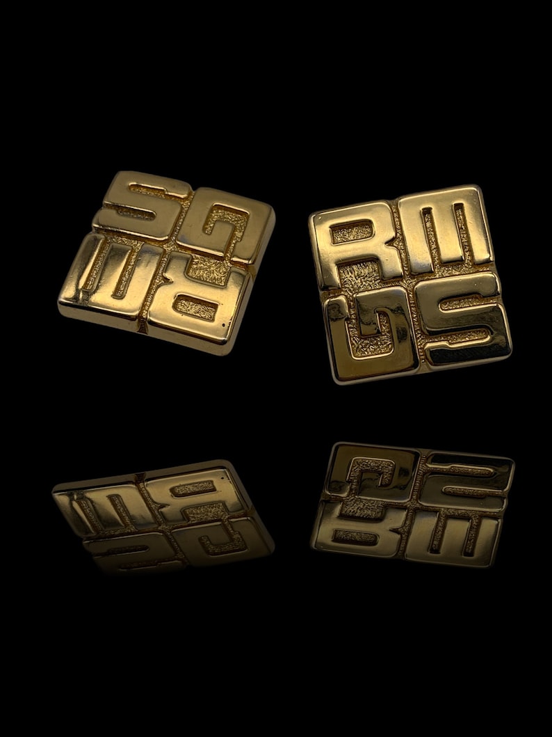 May include: A pair of gold-toned square earrings with a geometric design. The earrings feature a repeating pattern of the letters "GS" in a raised, textured style.