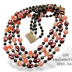 May include: A multi-strand necklace featuring alternating beads of black, pink, and peach hues. The necklace has a decorative clasp and is labeled "GM Giuliano Fratti 1950, Italy."