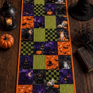 May include: A rectangular quilted table runner featuring a patchwork design of Halloween-themed fabric squares. The pattern includes illustrations of black cats, orange pumpkins, bats, crescent moons, haunted houses, and green and black checkerboard.