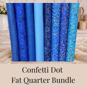 May include: A bundle of rolled fabric fat quarters in various shades of blue. The fabrics feature patterns like polka dots, swirls, and floral designs. The text "Confetti Dot Fat Quarter Bundle" is displayed below the fabrics.