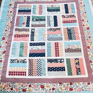 May include: A handmade quilt with a patchwork design. The quilt features rectangular blocks in various colors and patterns, including floral, stripes, and solid colors. The border is a floral print with a light blue background. The quilt is approximately 80 inches by 90 inches.