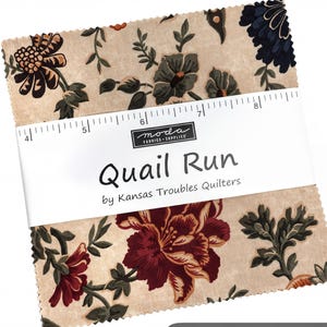 May include: A stack of square fabric pieces with a beige background and floral patterns in dark red, navy blue, and olive green. A white paper band wraps around the center, featuring the text "Quail Run by Kansas Troubles Quilters" and a ruler.