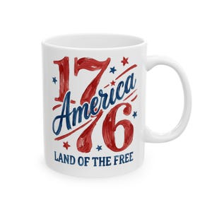 May include: A white ceramic mug featuring a red and blue painted design. The text reads 1776, America, and LAND OF THE FREE, accented with small red and blue stars. The design has a brushstroke texture and is centered on the front of the mug.