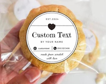 Könnte beinhalten: Ein weißer runder Aufkleber mit schwarzem Text, der "EST. 2024", "Custom Text", "BY YOUR NAME", "customtext", "(510) 123 3456", "made from scratch" und "with love" lautet. Der Aufkleber hat ein schwarzes Herz mit einem Biss. Der Aufkleber befindet sich auf einem braunen Keks.