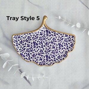 May include: A decorative ceramic tray in a fan shape, featuring a blue leaf pattern on a white background. The tray has a gold-colored rim and handle. The text "Tray Style 5" is visible on the top left.