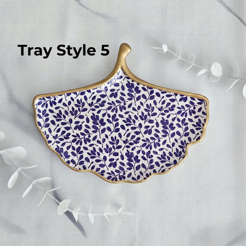 May include: A decorative ceramic tray in a fan shape, featuring a blue leaf pattern on a white background. The tray has a gold-colored rim and handle. The text "Tray Style 5" is visible on the top left.