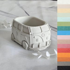 May include: A white, hollow, van-shaped planter with a textured surface. The design features a front bumper, circular headlights, and side windows. A vertical color palette strip is displayed on the right side, showing various solid color options.