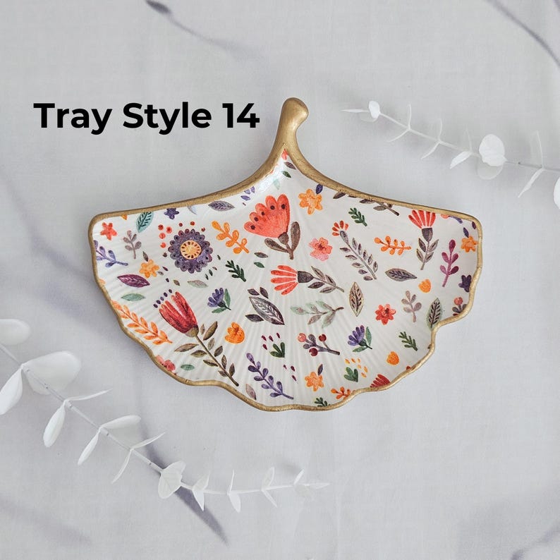 May include: A decorative, leaf-shaped tray with a gold rim and handle. The white surface is adorned with colorful floral and leaf patterns in orange, purple, and green. The text "Tray Style 14" is visible in the upper left corner.
