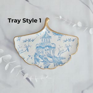 May include: A white and blue decorative tray in a leaf shape with a gold trim. The tray features a blue and white pagoda and bird design. The text "Tray Style 1" is printed on the tray.