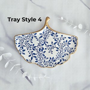 May include: A decorative ceramic tray in a fan shape, featuring a white background with a blue leaf pattern. The rim and handle are trimmed with gold. The text "Tray Style 4" is visible.