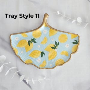 May include: A light blue, ginkgo leaf-shaped tray with a gold rim and handle. The tray is decorated with yellow lemons, green leaves, and white flowers. The text "Tray Style 11" is printed on the top left.