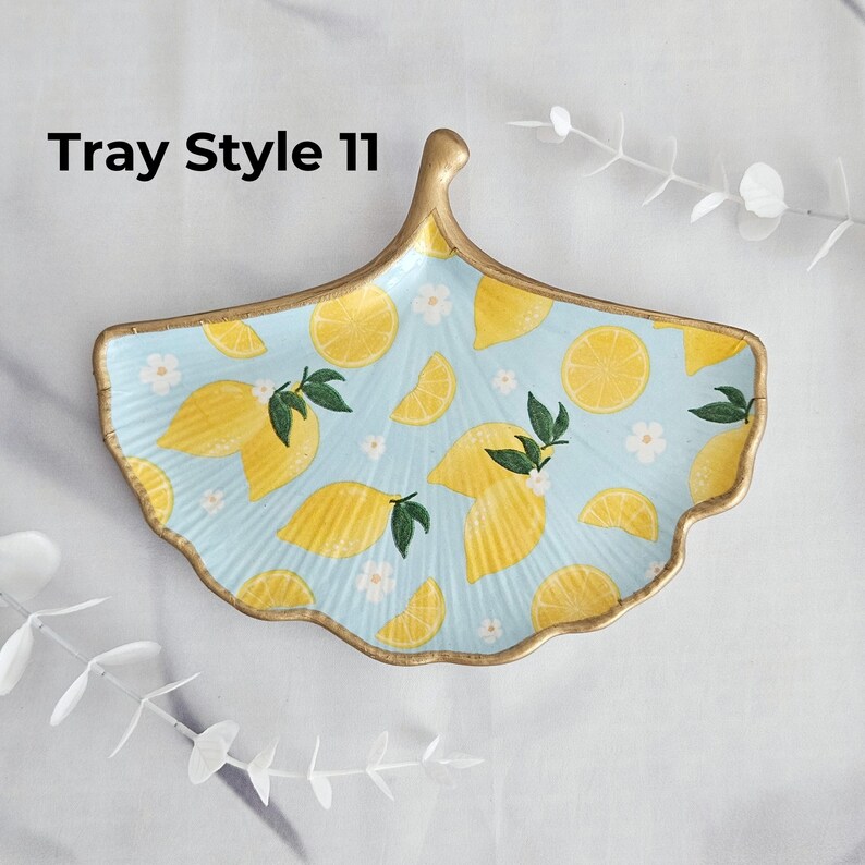 May include: A light blue, ginkgo leaf-shaped tray with a gold rim and handle. The tray is decorated with yellow lemons, green leaves, and white flowers. The text "Tray Style 11" is printed on the top left.