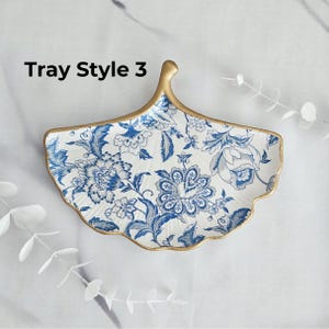 May include: A decorative, leaf-shaped tray with a white background and blue floral patterns. The tray has a gold-colored rim and handle. The text "Tray Style 3" is visible on the tray.