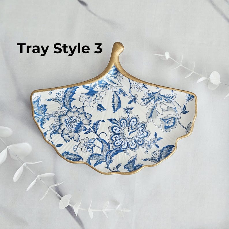May include: A decorative, leaf-shaped tray with a white background and blue floral patterns. The tray has a gold-colored rim and handle. The text "Tray Style 3" is visible on the tray.
