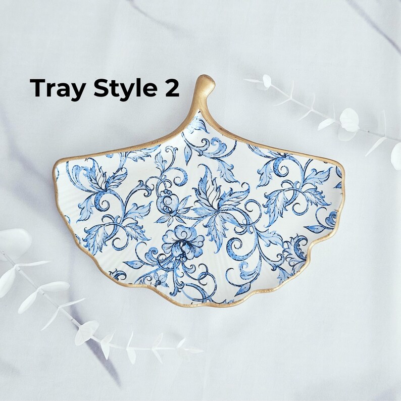 May include: A white ceramic tray with a blue floral pattern and gold trim. The tray is shaped like a ginkgo leaf and has the text "Tray Style 2" in black.