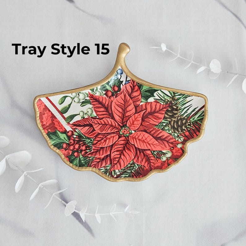 May include: A decorative, ginkgo leaf-shaped tray with a gold trim. The tray features a poinsettia and pinecone design with the text "Tray Style 15". The tray is perfect for serving or as a decorative accent.
