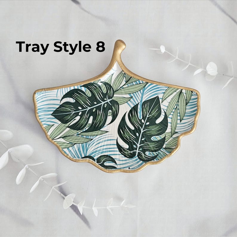 May include: Ginkgo leaf-shaped decorative tray with a gold rim. The tray features a tropical leaf pattern in shades of green and blue on a white background. The text "Tray Style 8" is visible on the upper left.