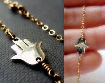 May include: A gold chain necklace with a silver hamsa hand charm. The hamsa hand is a symbol of protection and good luck.