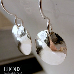 May include: A pair of silver hammered disc earrings with a simple hook closure. The earrings are handmade and have a textured surface.
