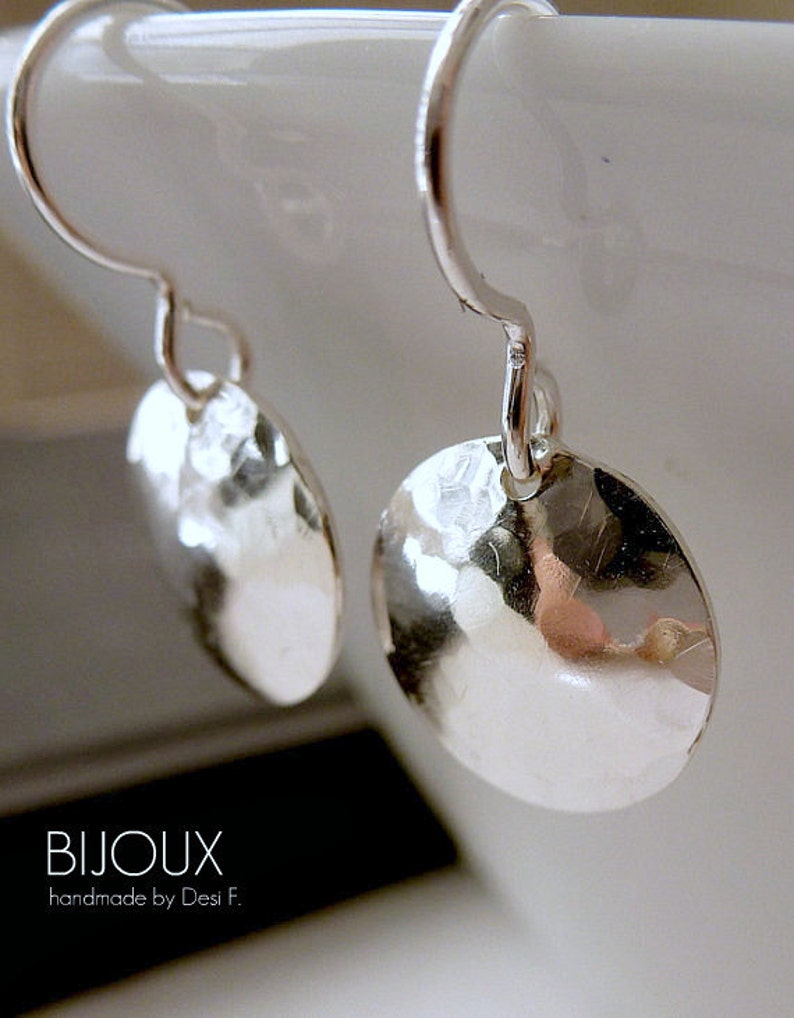 May include: A pair of silver hammered disc earrings with a simple hook closure. The earrings are handmade and have a textured surface.