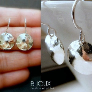 May include: A pair of silver earrings with hammered round discs. The earrings have a simple, minimalist design.