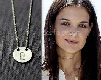 May include: A silver necklace with a round pendant featuring the letter "B" engraved on it. The necklace is worn by a woman with long dark hair.