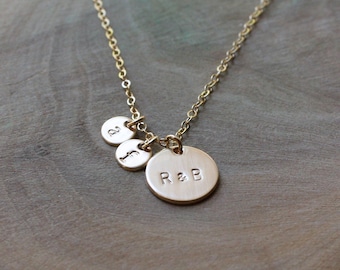 May include: Gold necklace with three round charms. The largest charm is engraved with "R&B". The smaller charms are engraved with "J" and "D".