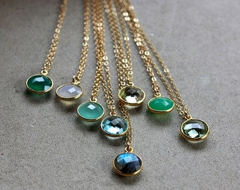 May include: A set of gold necklaces with various gemstone pendants, including green, blue, and clear stones. The necklaces are layered and feature different lengths.